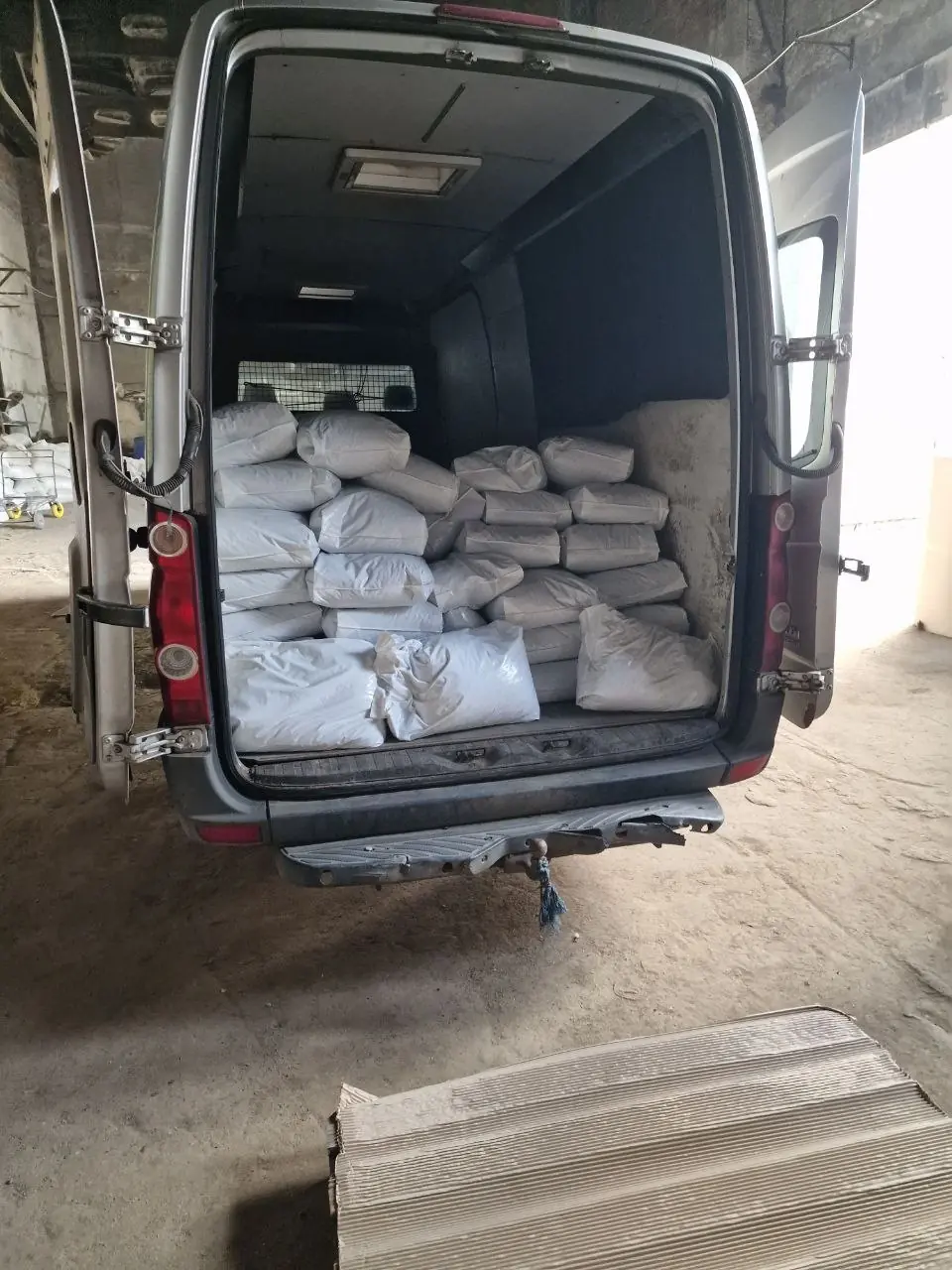 The shelter van with its doors open, loaded with white bags of dog food, inside the supplier's warehouse