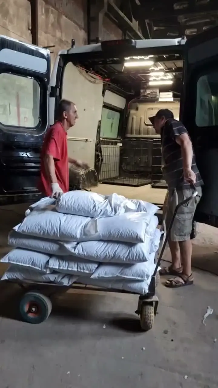 Two men loading a trolley of white food bags into the shelter van at the supplier's warehouse