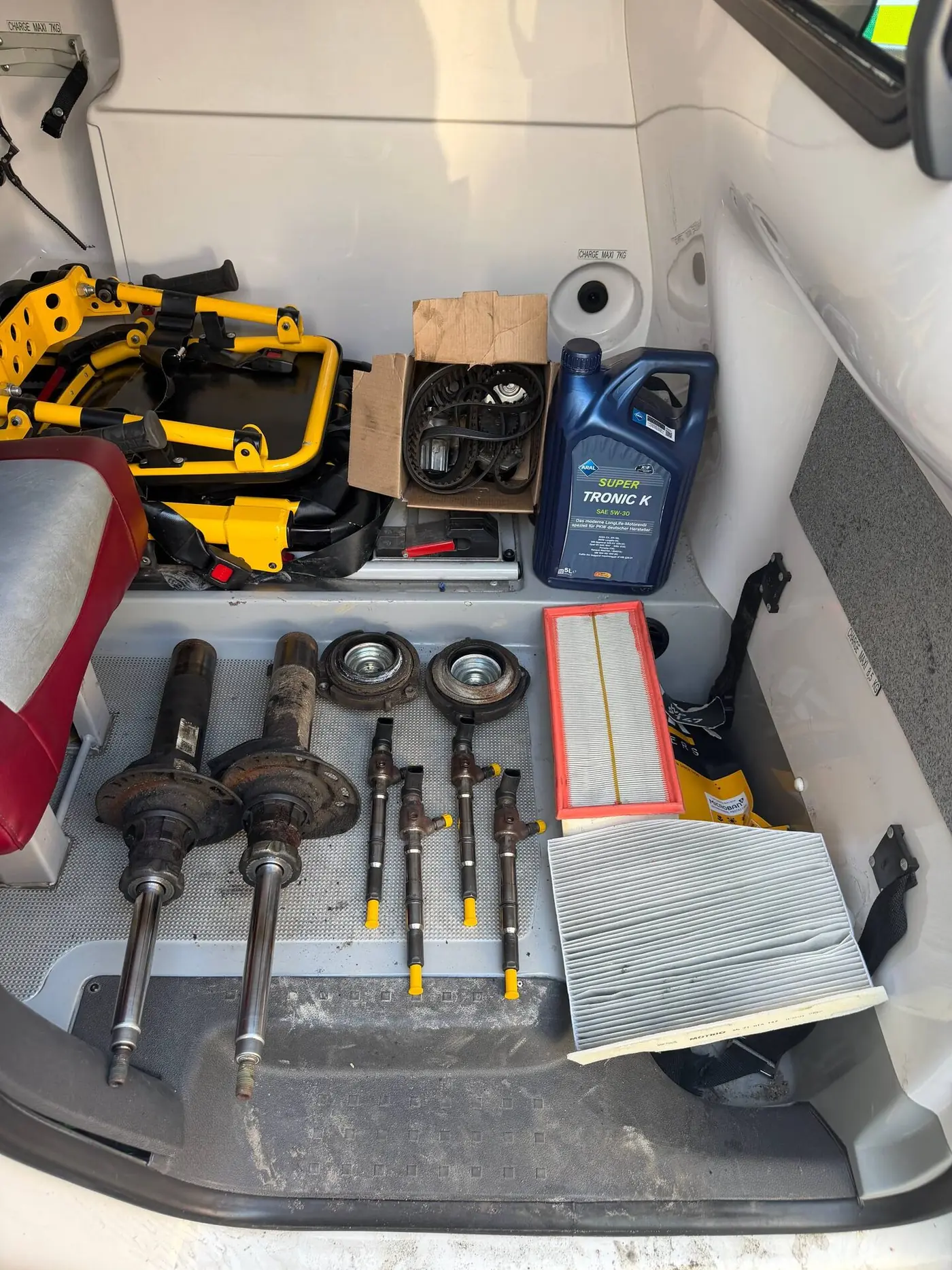 Old front struts, strut mounts and four used fuel injectors laid out on the rear floor of the Caddy, with filters, a bottle of engine oil and the timing belt kit beside them